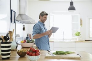 mature man in his kitchen reading recipe on his digital tablet